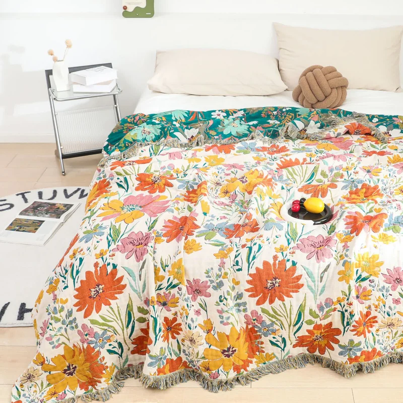 Wendbare Sofadecke aus Baumwollgaze mit Quasten und leuchtendem Blumenmuster